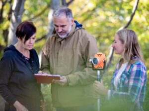 Property owners meeting with a surveyor during a land survey on a wooded property